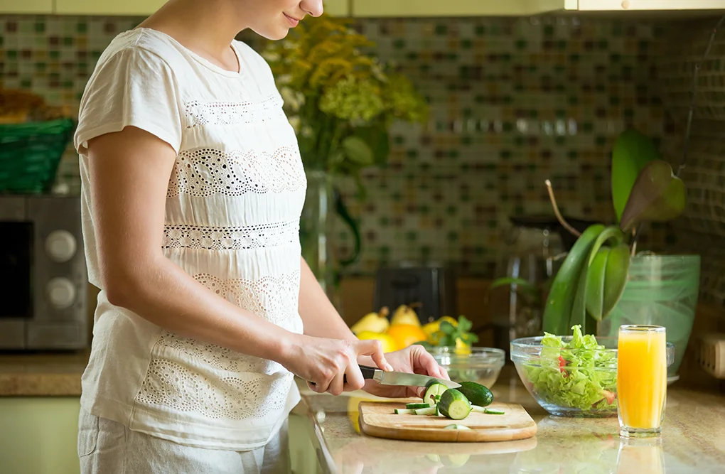 woman-cutting-cucumbers-salad-kitchen